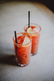 Two Bloody Mary cocktails with lemon wedges and straws on a wooden surface.